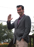 A man in a suit waves at the camera.